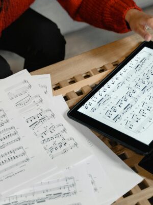 A person reviewing and composing sheet music using both paper and digital formats on a table.